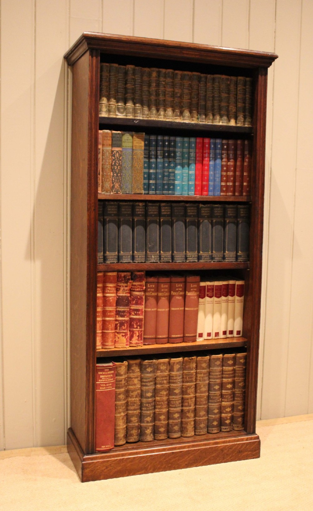 A tall late Victorian open oak bookcase featuring five adjustable shelves filled with books, a moulded top cornice, and a solid plinth base. View V