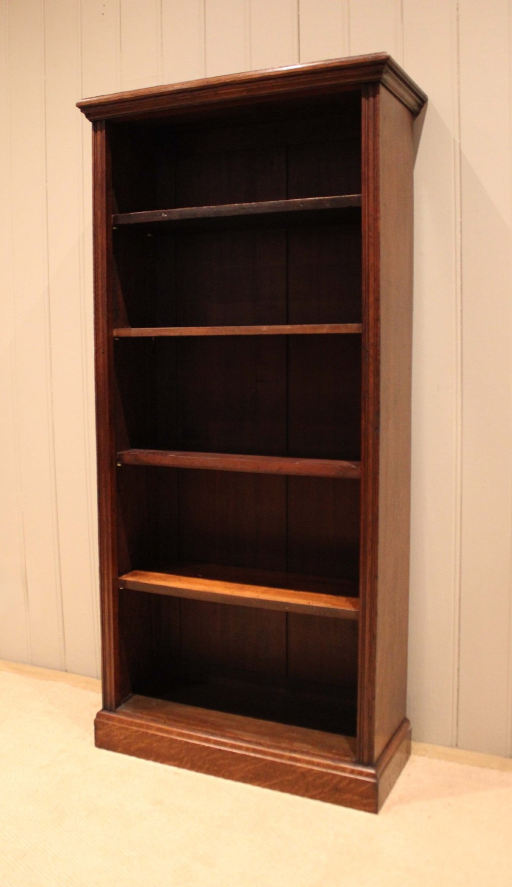A tall late Victorian open oak bookcase featuring five adjustable shelves filled with books, a moulded top cornice, and a solid plinth base. View VI