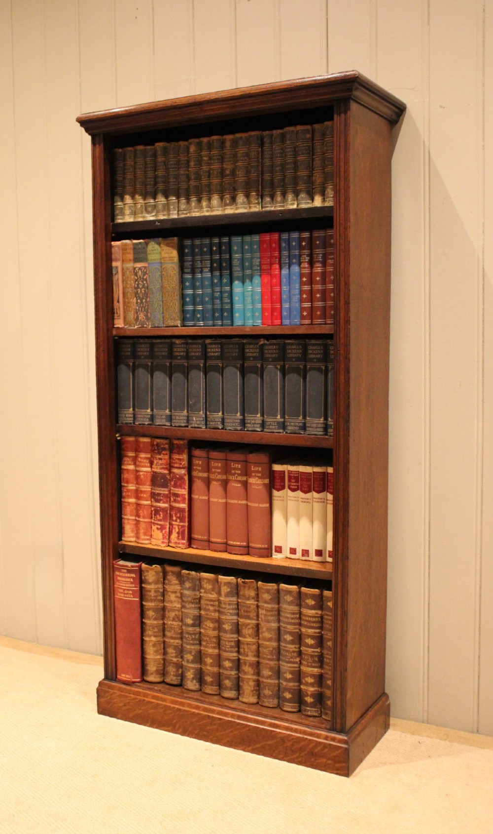 A tall late Victorian open oak bookcase featuring five adjustable shelves filled with books, a moulded top cornice, and a solid plinth base. View VII