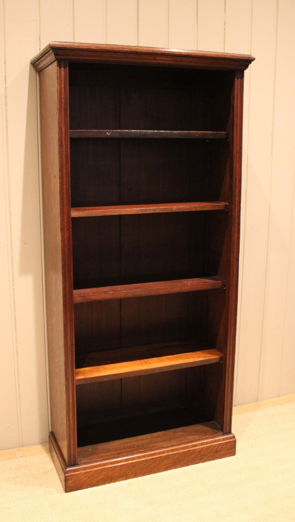 A tall late Victorian open oak bookcase featuring five adjustable shelves filled with books, a moulded top cornice, and a solid plinth base. View VIII
