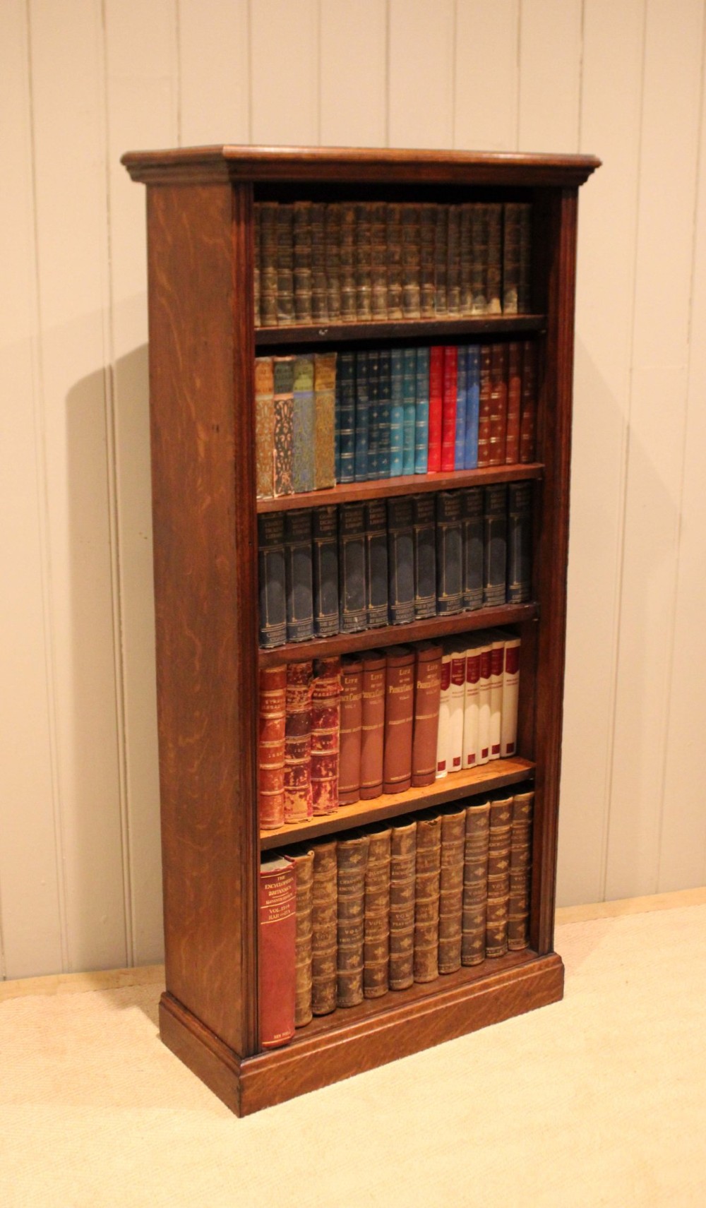 A tall late Victorian open oak bookcase featuring five adjustable shelves filled with books, a moulded top cornice, and a solid plinth base. View IX