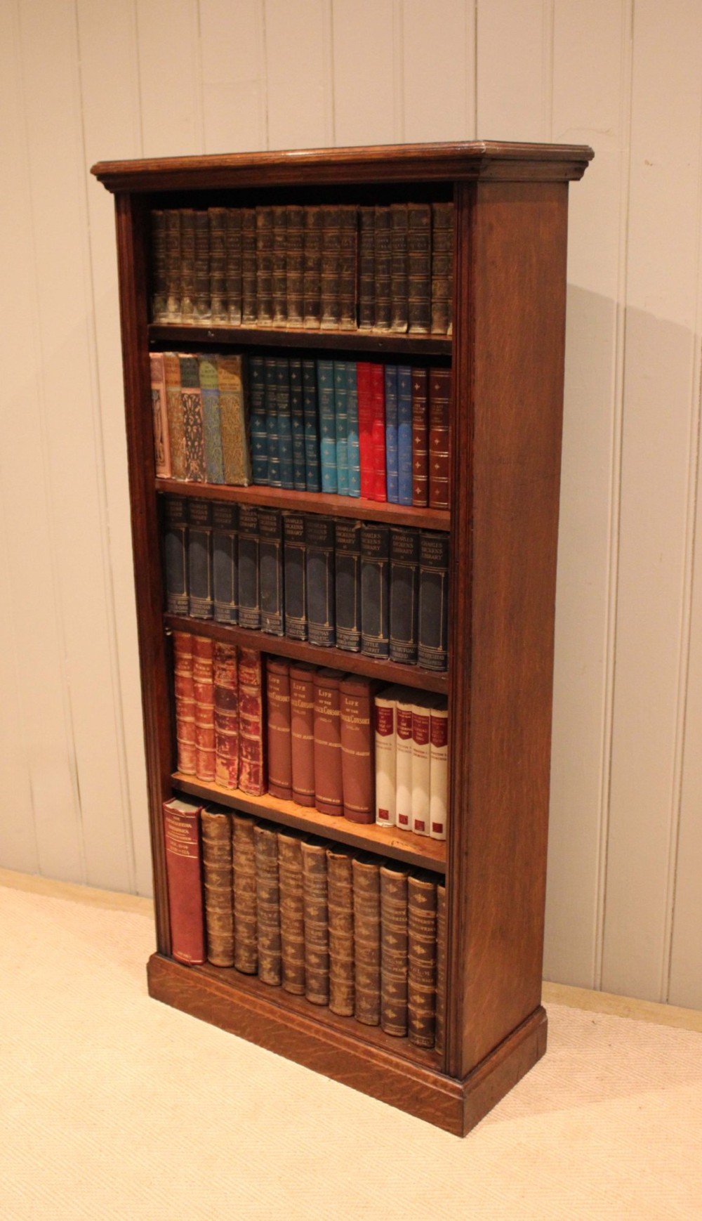 A tall late Victorian open oak bookcase featuring five adjustable shelves filled with books, a moulded top cornice, and a solid plinth base. View XI
