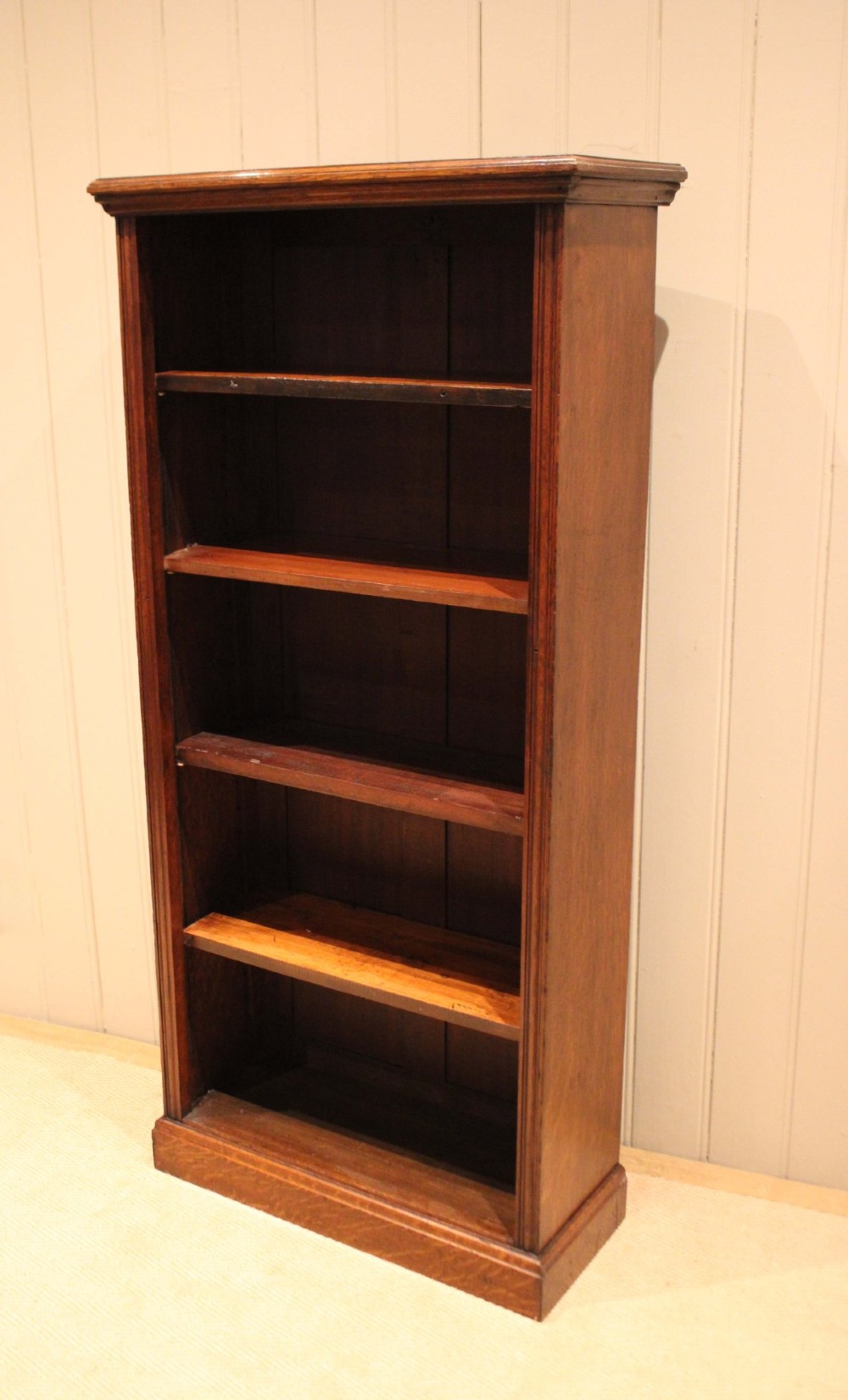 A tall late Victorian open oak bookcase featuring five adjustable shelves filled with books, a moulded top cornice, and a solid plinth base. View XII