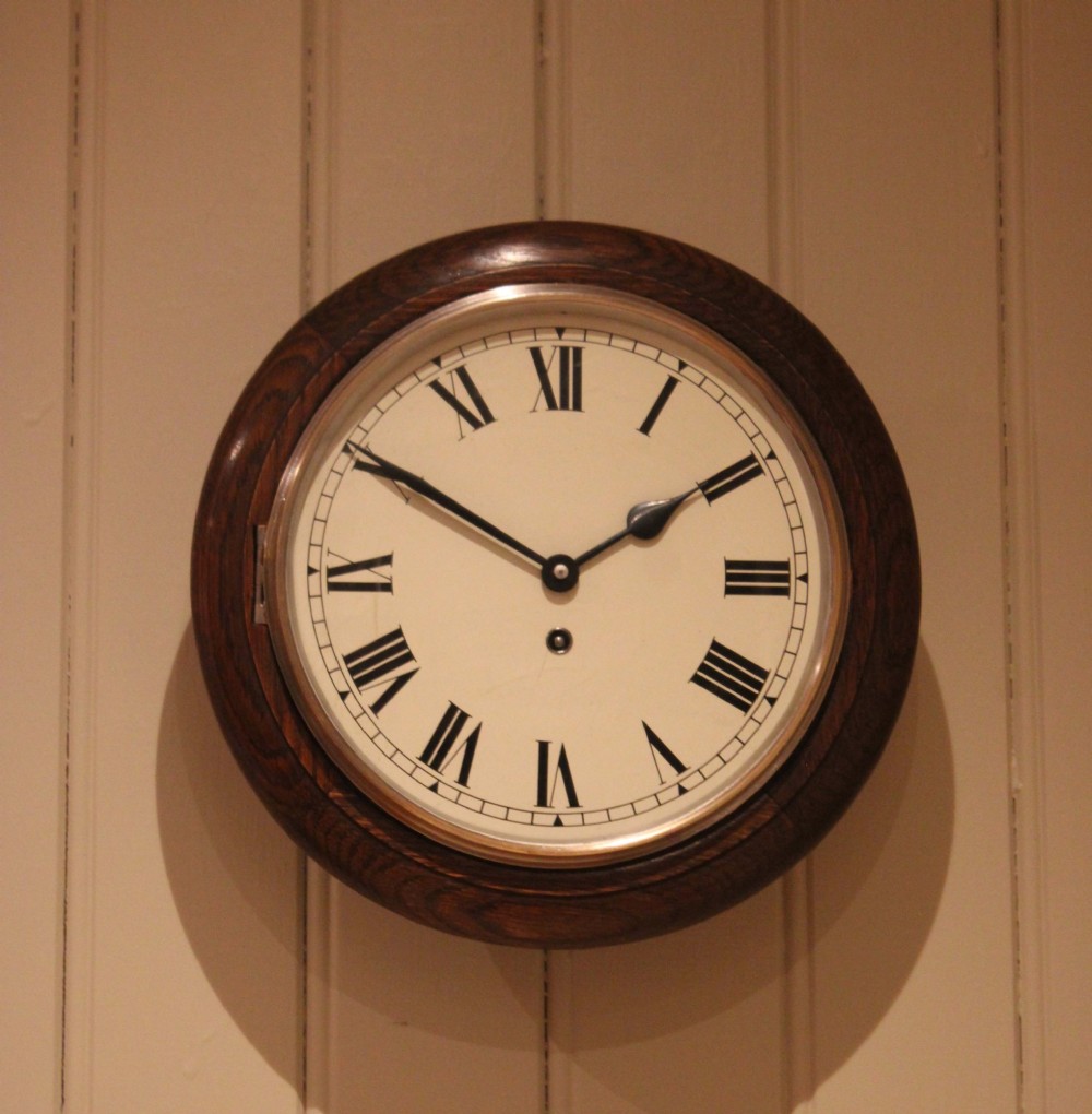 A circular early 20th-century wall clock featuring a moulded dark oak frame, a brass bezel, and a white dial face with black Roman numerals. View II