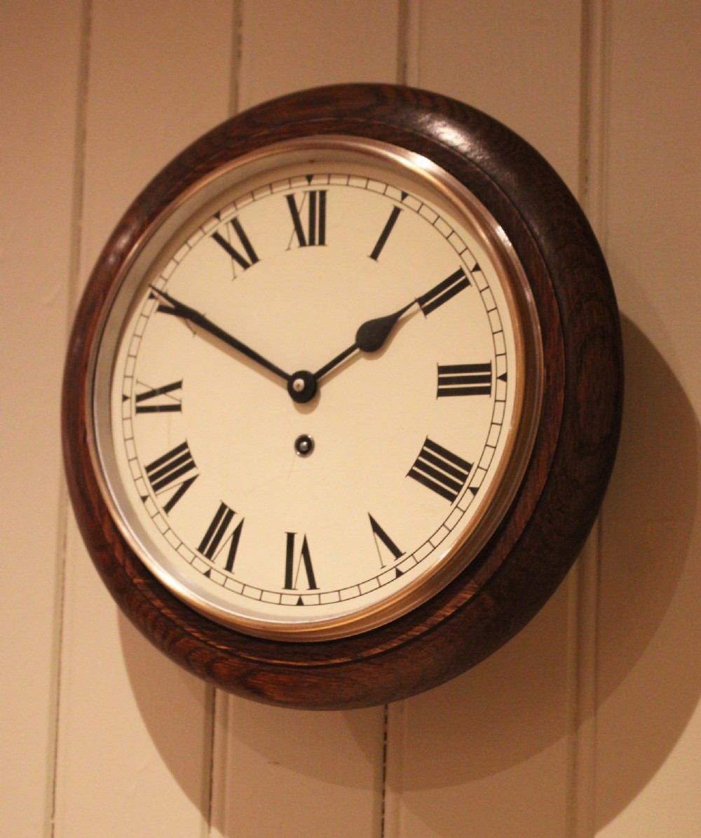 A circular early 20th-century wall clock featuring a moulded dark oak frame, a brass bezel, and a white dial face with black Roman numerals. View III