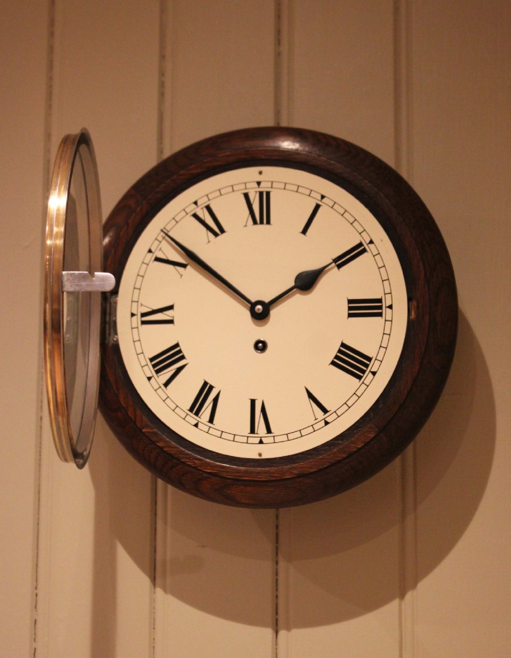A circular early 20th-century wall clock featuring a moulded dark oak frame, a brass bezel, and a white dial face with black Roman numerals. View VII
