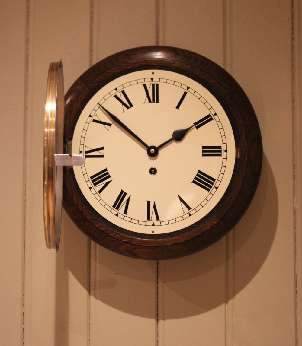 A circular early 20th-century wall clock featuring a moulded dark oak frame, a brass bezel, and a white dial face with black Roman numerals. View IX