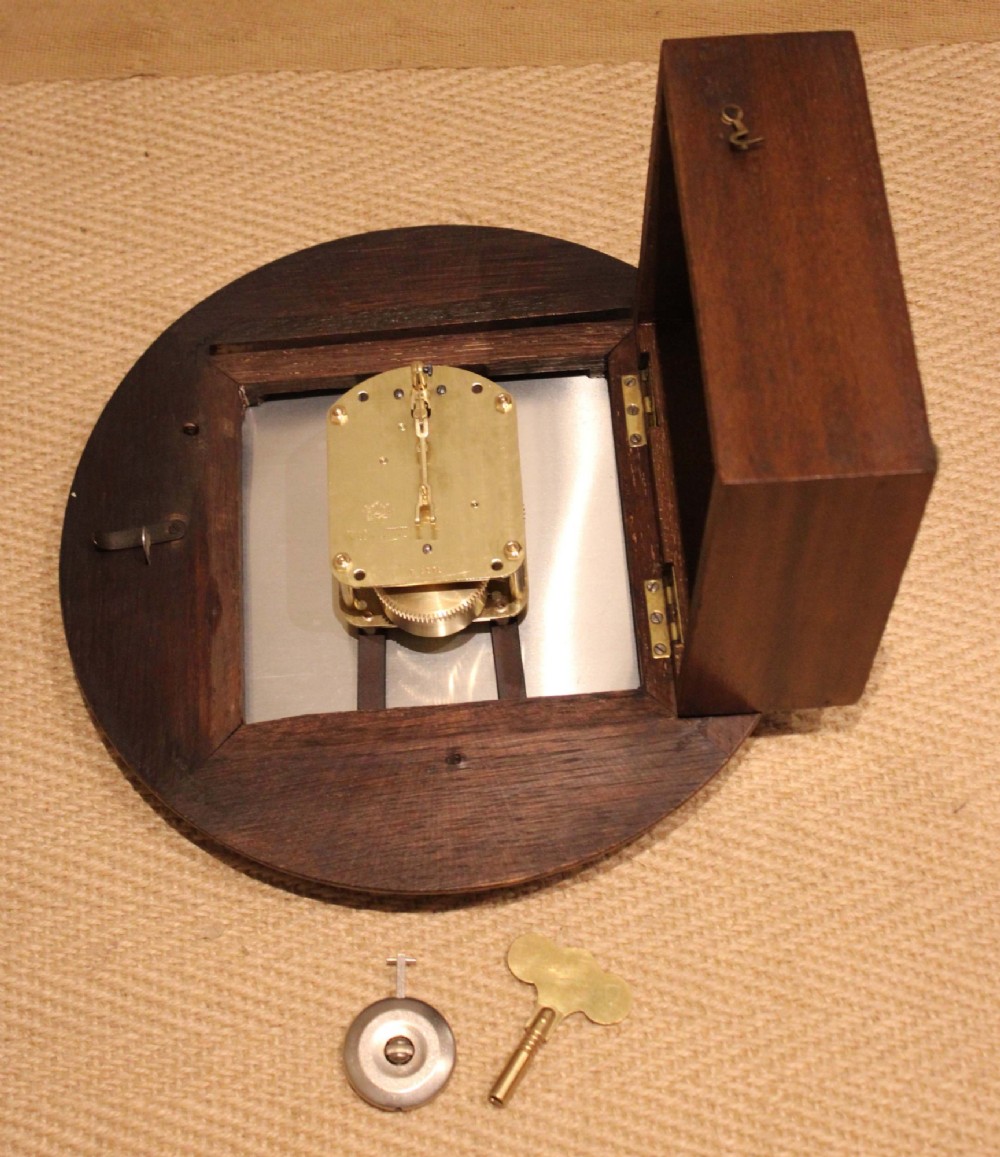 A circular early 20th-century wall clock featuring a moulded dark oak frame, a brass bezel, and a white dial face with black Roman numerals. View XIII