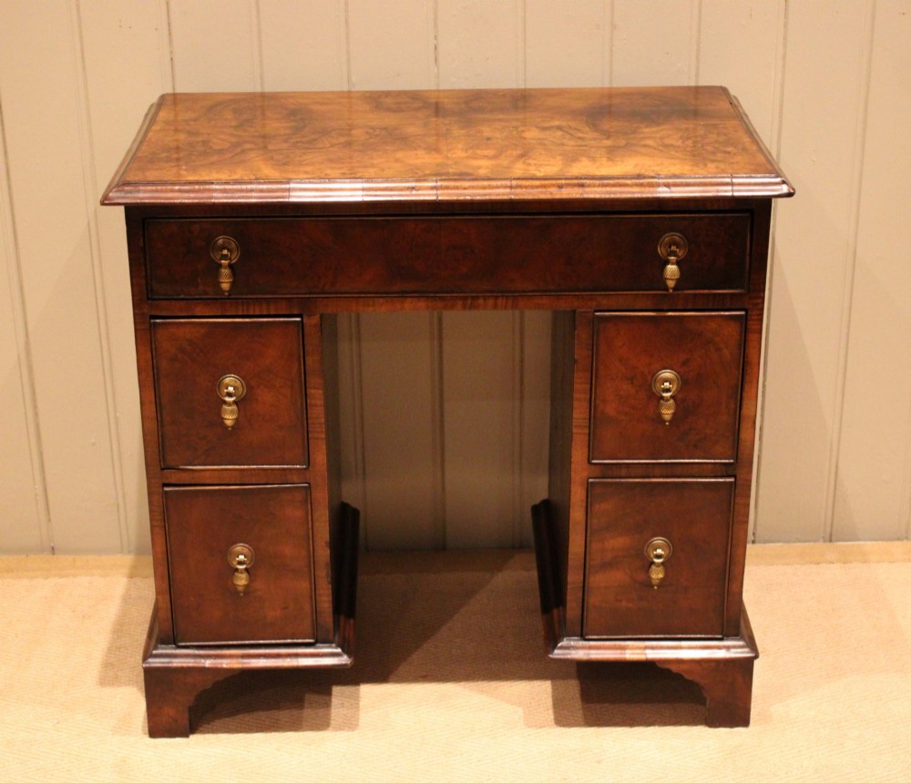 A small proportioned burr walnut pedestal desk featuring five drawers with brass drop handles and bracket feet.