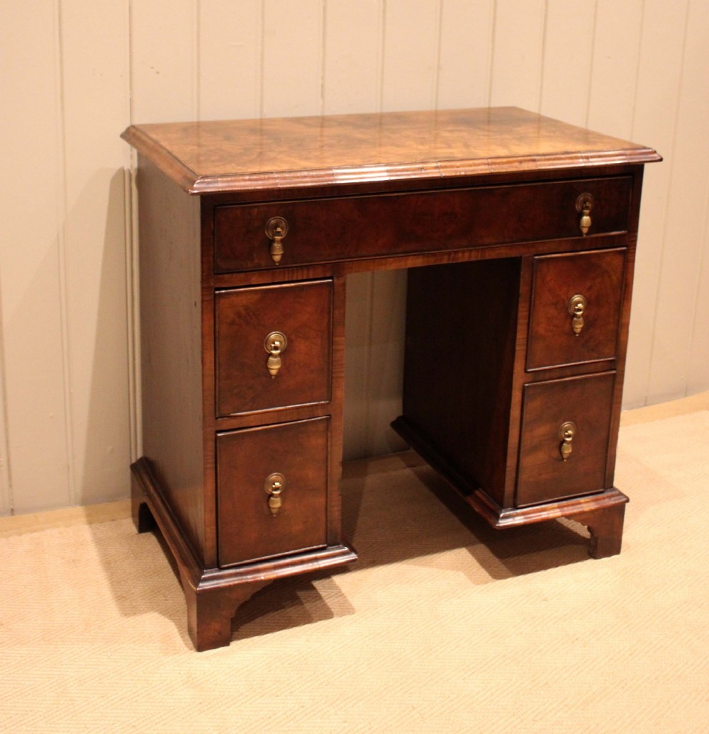 A small proportioned burr walnut pedestal desk featuring five drawers with brass drop handles and bracket feet. View II