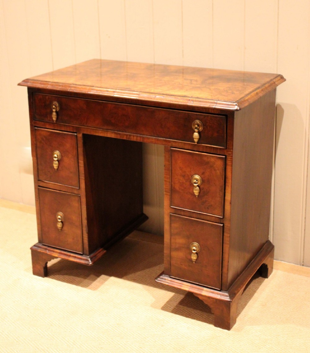 A small proportioned burr walnut pedestal desk featuring five drawers with brass drop handles and bracket feet. View III