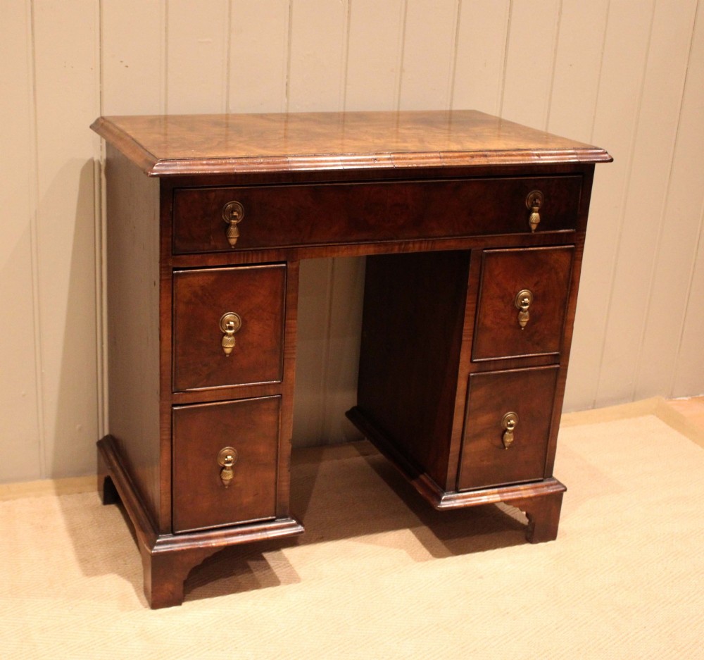 A small proportioned burr walnut pedestal desk featuring five drawers with brass drop handles and bracket feet. View V