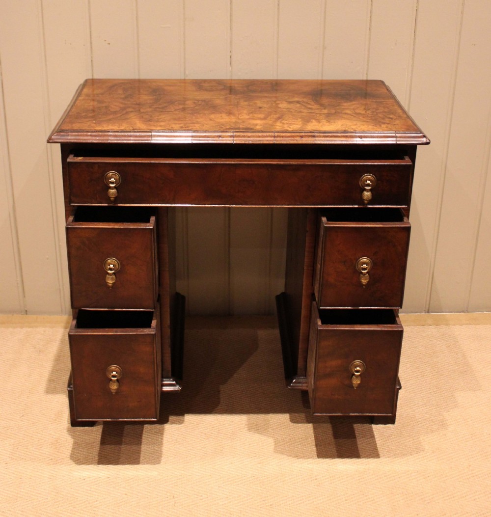 A small proportioned burr walnut pedestal desk featuring five drawers with brass drop handles and bracket feet. View VI