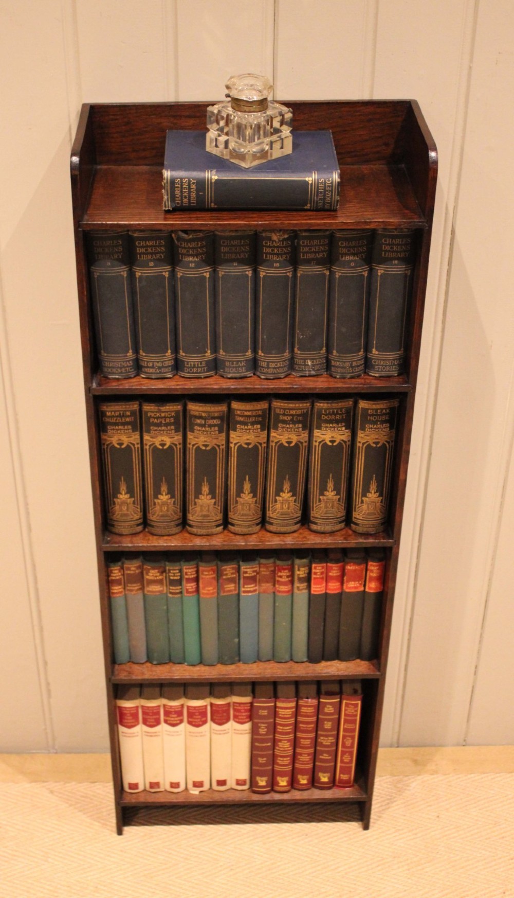 A narrow 1920s dark oak open bookcase featuring four fixed shelves filled with vintage books. View III
