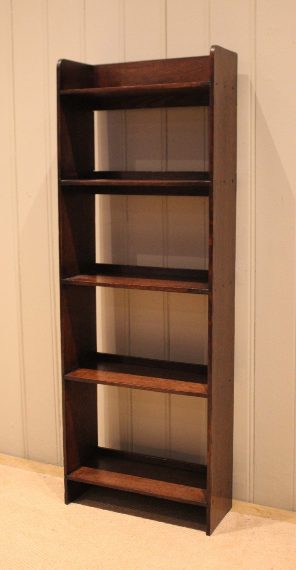 A narrow 1920s dark oak open bookcase featuring four fixed shelves filled with vintage books. View IV