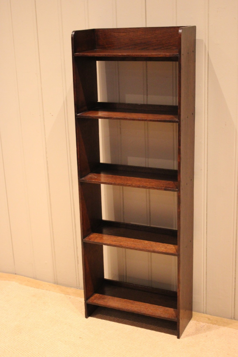 A narrow 1920s dark oak open bookcase featuring four fixed shelves filled with vintage books. View VI