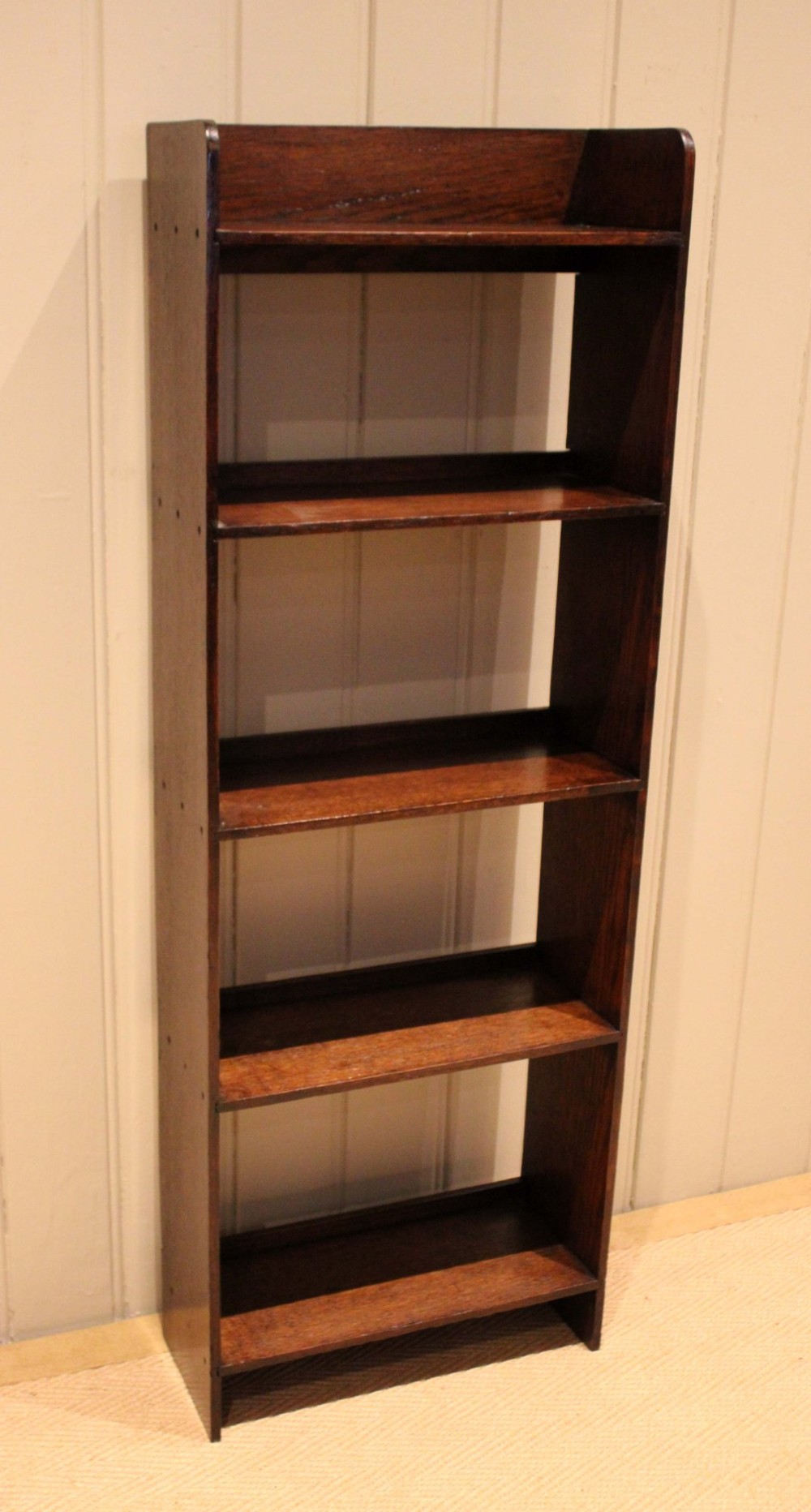 A narrow 1920s dark oak open bookcase featuring four fixed shelves filled with vintage books. View VIII
