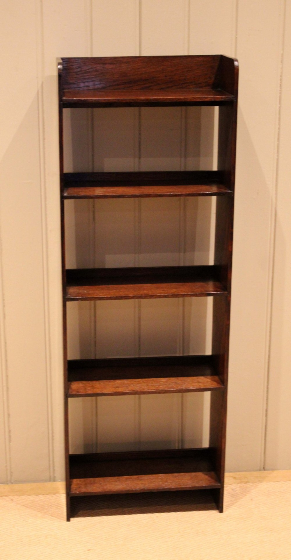 A narrow 1920s dark oak open bookcase featuring four fixed shelves filled with vintage books. View X
