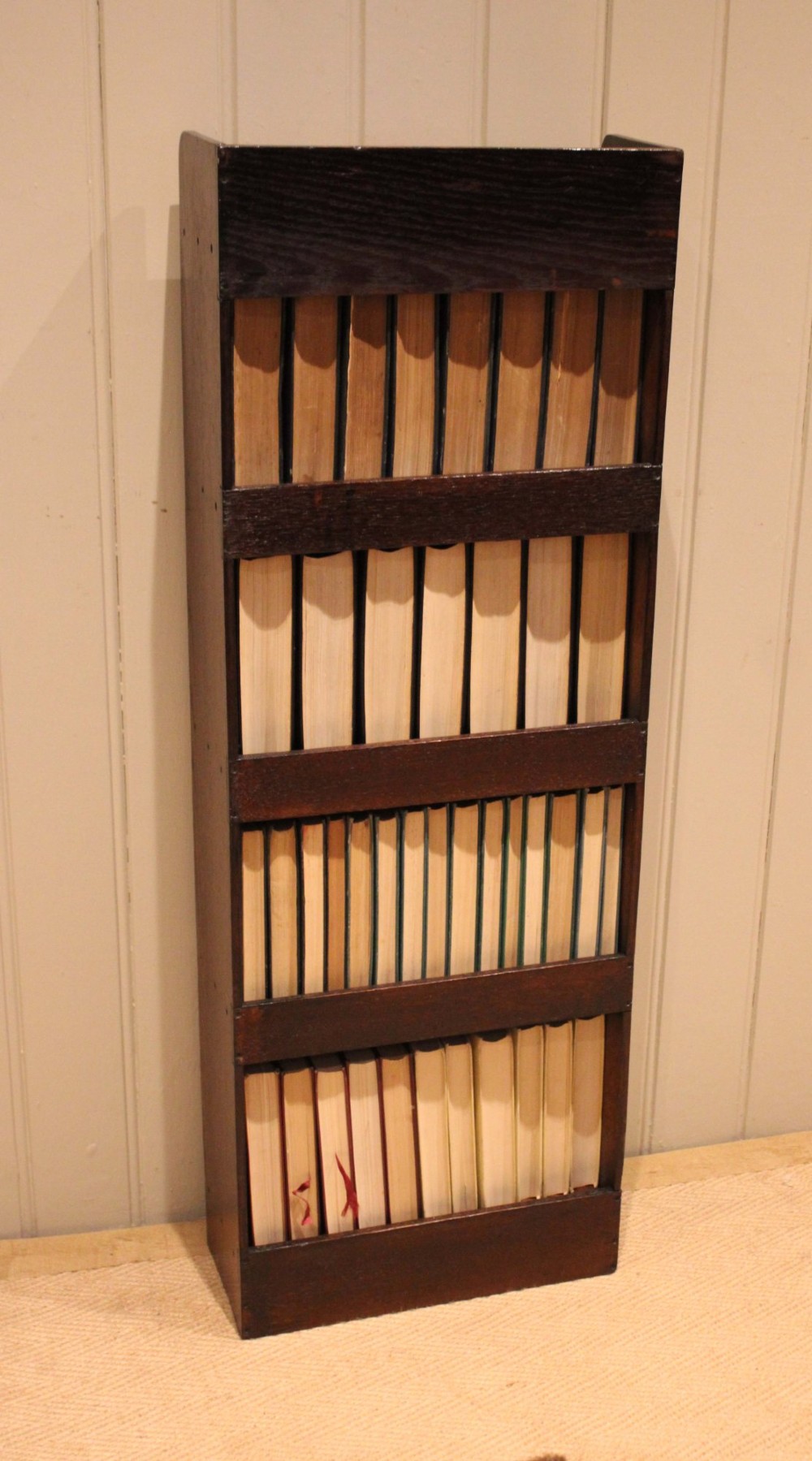 A narrow 1920s dark oak open bookcase featuring four fixed shelves filled with vintage books. View XII