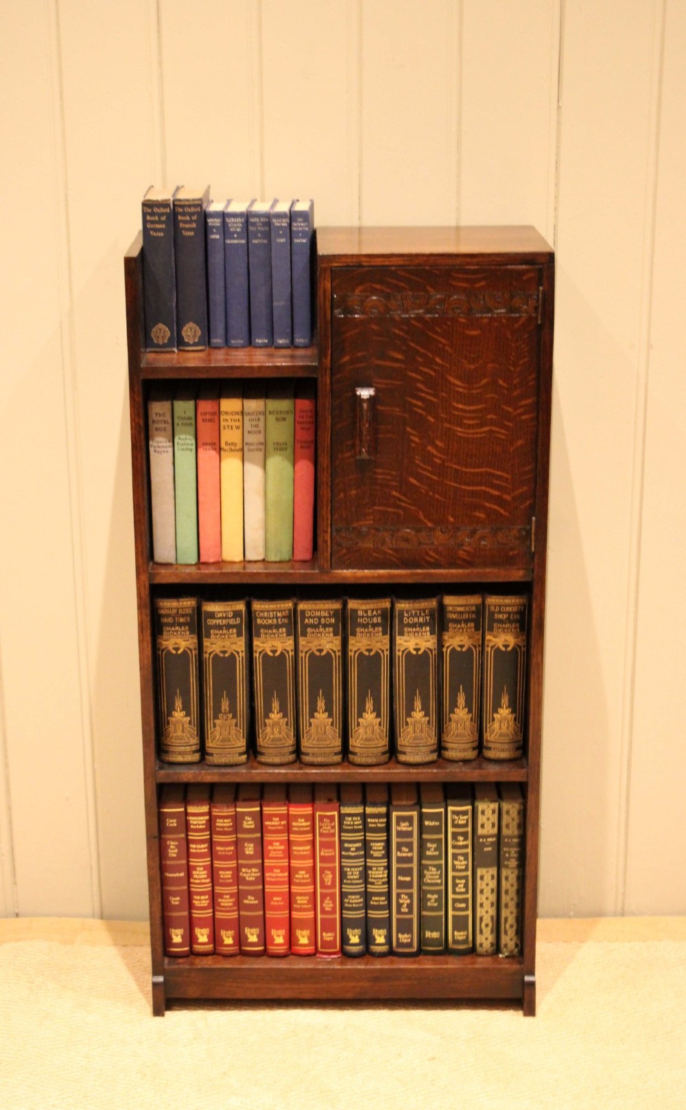 A dark oak Art Deco bookcase with open shelves on the left side, a small carved single door cabinet on the right, and two lower full-width shelves.
