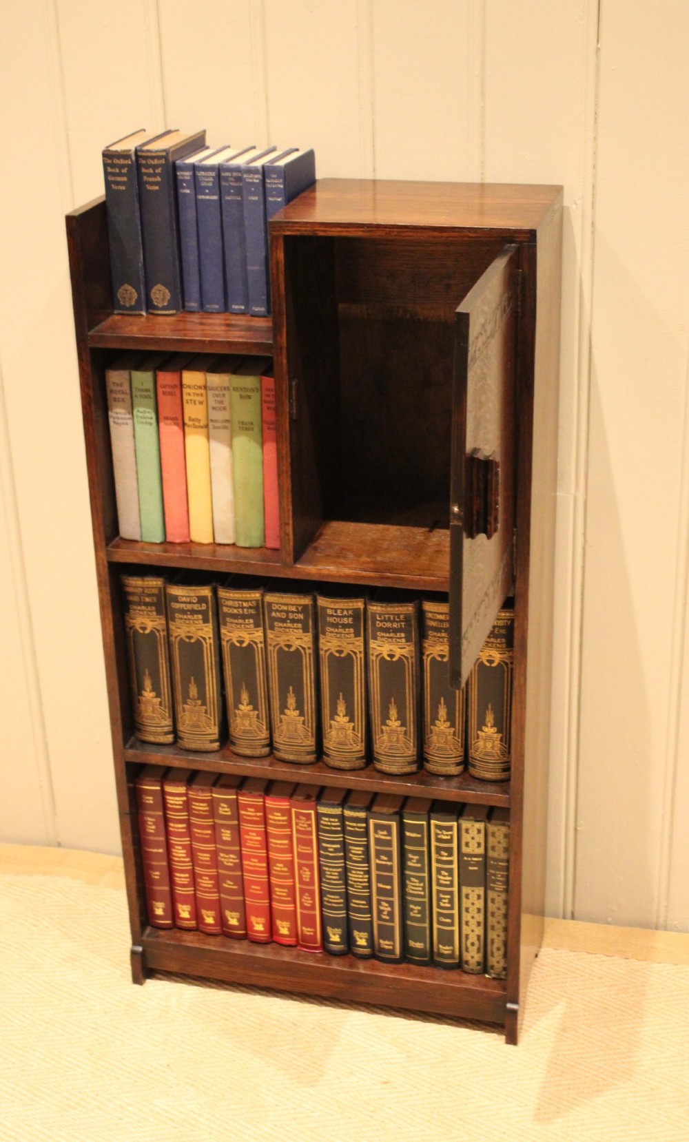 A dark oak Art Deco bookcase with open shelves on the left side, a small carved single door cabinet on the right, and two lower full-width shelves. View III