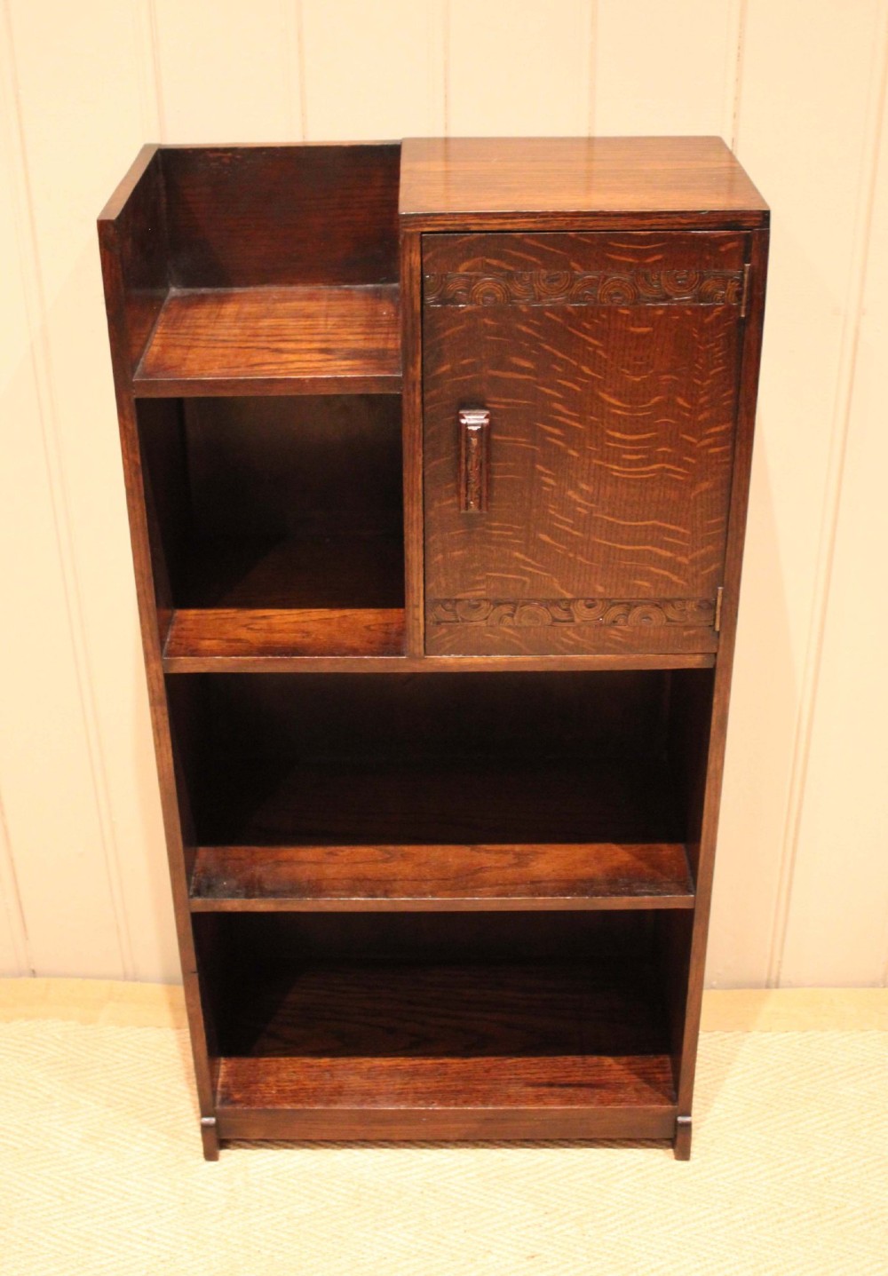 A dark oak Art Deco bookcase with open shelves on the left side, a small carved single door cabinet on the right, and two lower full-width shelves. View IV
