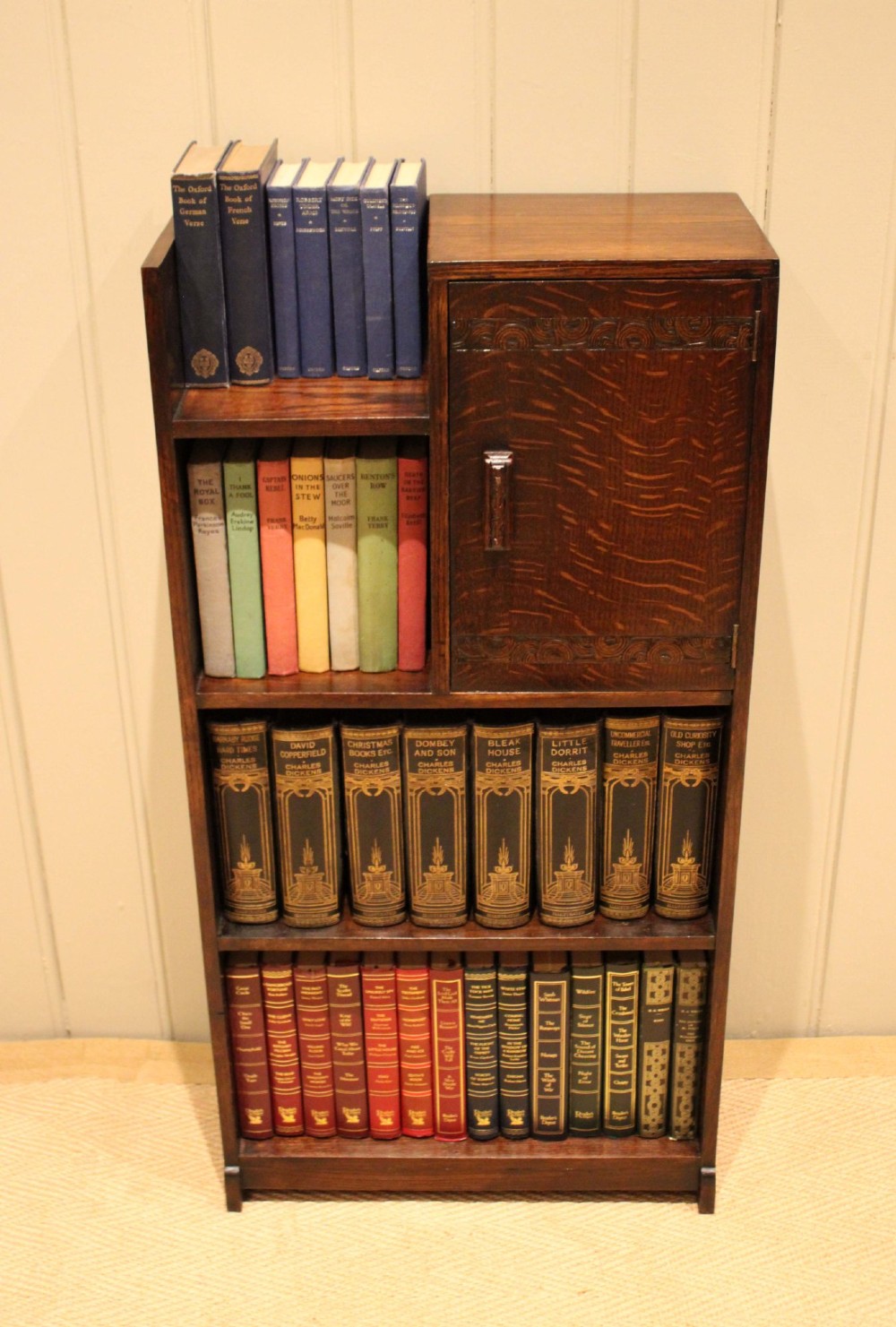 A dark oak Art Deco bookcase with open shelves on the left side, a small carved single door cabinet on the right, and two lower full-width shelves. View V