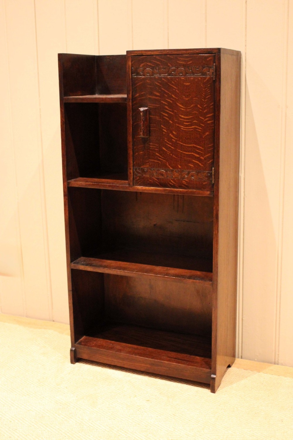 A dark oak Art Deco bookcase with open shelves on the left side, a small carved single door cabinet on the right, and two lower full-width shelves. View VI