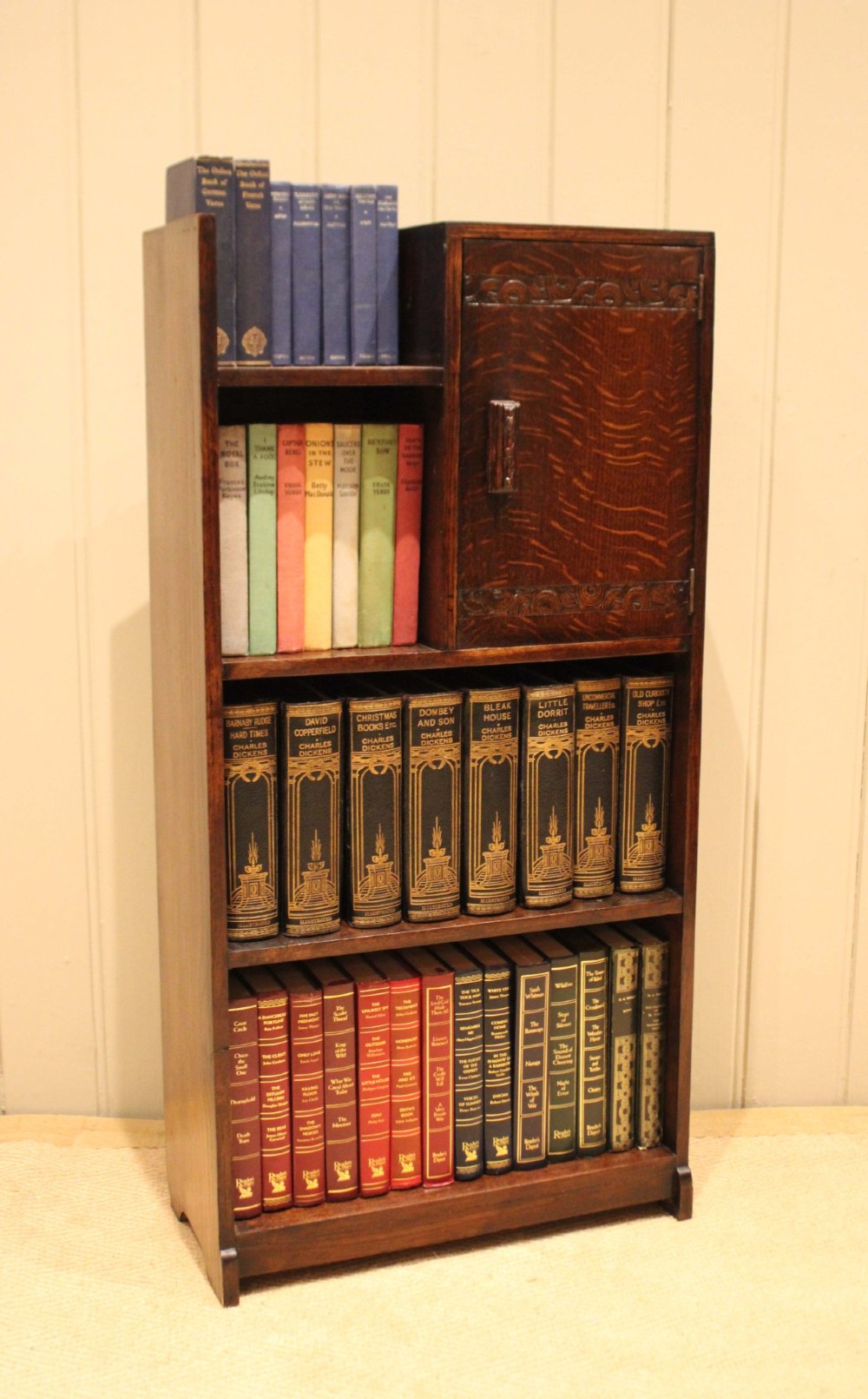 A dark oak Art Deco bookcase with open shelves on the left side, a small carved single door cabinet on the right, and two lower full-width shelves. View VII