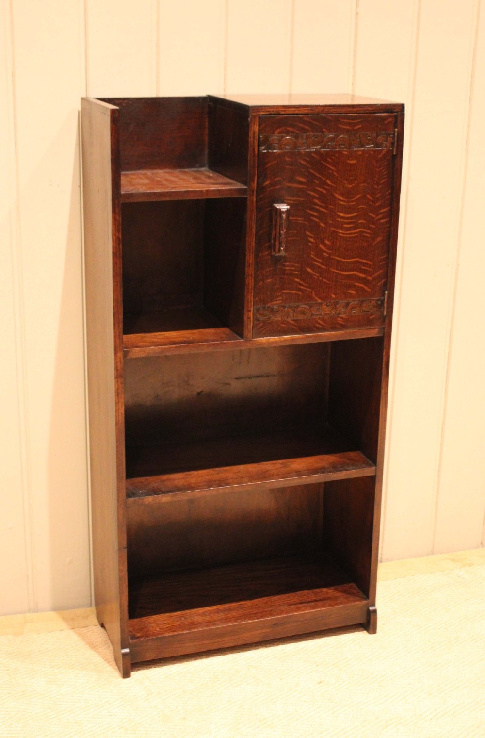 A dark oak Art Deco bookcase with open shelves on the left side, a small carved single door cabinet on the right, and two lower full-width shelves. View VIII