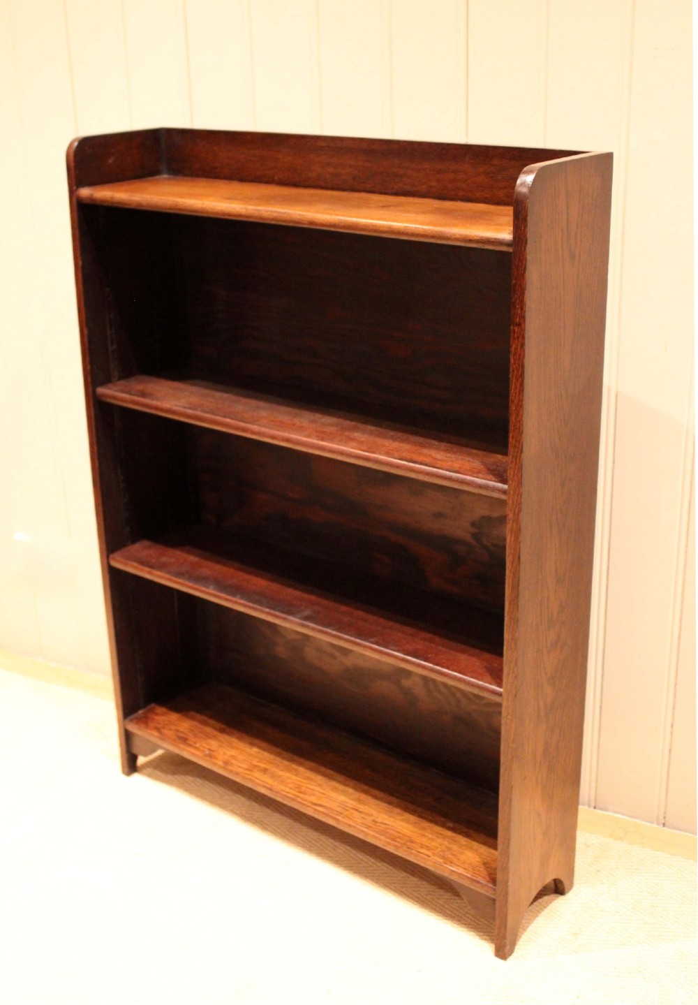 A dark brown oak open bookcase with three adjustable shelves, filled with vintage leather-bound books against a neutral panelled wall. View II