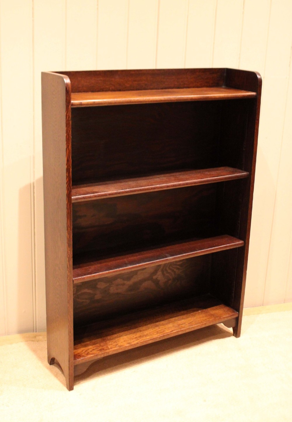 A dark brown oak open bookcase with three adjustable shelves, filled with vintage leather-bound books against a neutral panelled wall. View IV