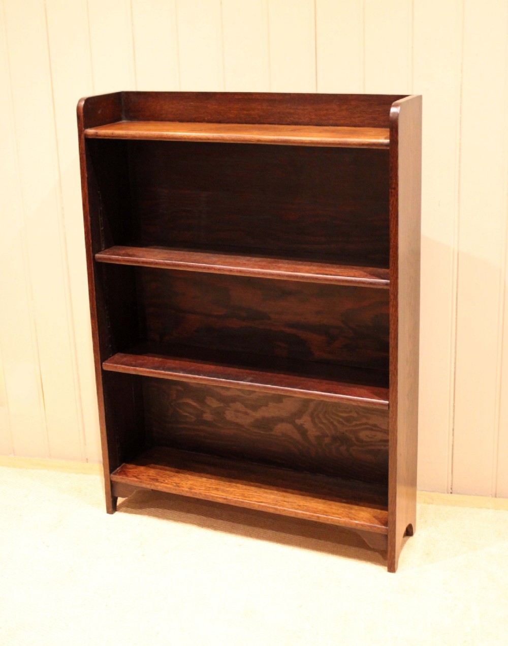 A dark brown oak open bookcase with three adjustable shelves, filled with vintage leather-bound books against a neutral panelled wall. View V