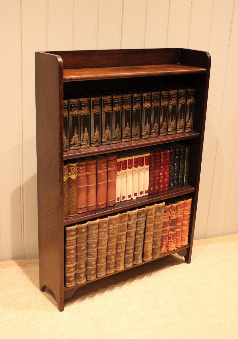 A dark brown oak open bookcase with three adjustable shelves, filled with vintage leather-bound books against a neutral panelled wall. View VII