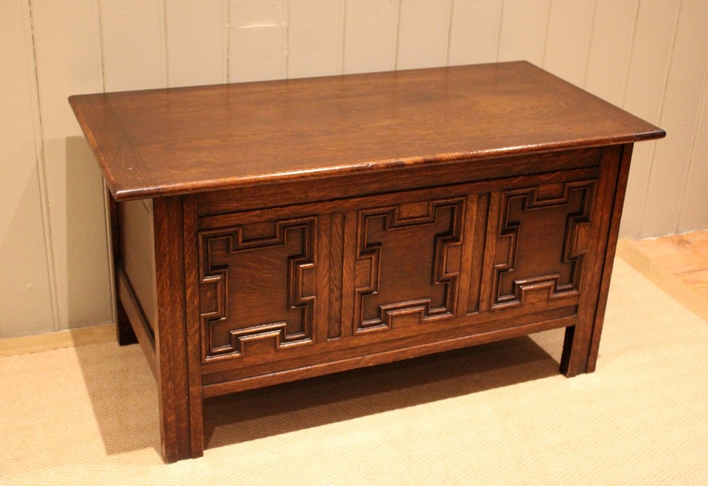 A dark oak coffer featuring three carved geometric recessed panels across the front and a flat hinged top lid.