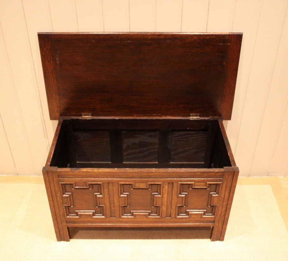 A dark oak coffer featuring three carved geometric recessed panels across the front and a flat hinged top lid. View IV