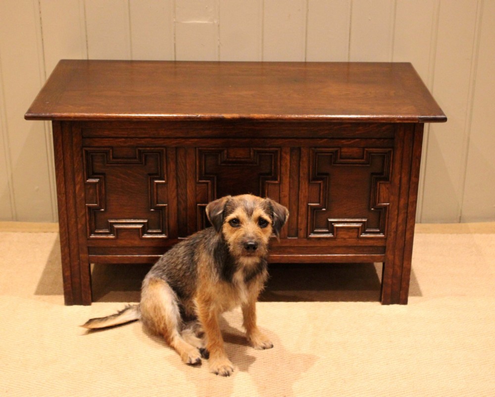 A dark oak coffer featuring three carved geometric recessed panels across the front and a flat hinged top lid. View V