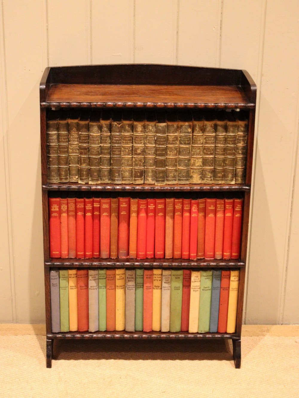 A small dark oak open bookcase with three fixed shelves and beaded edge moulding along each front shelf border.