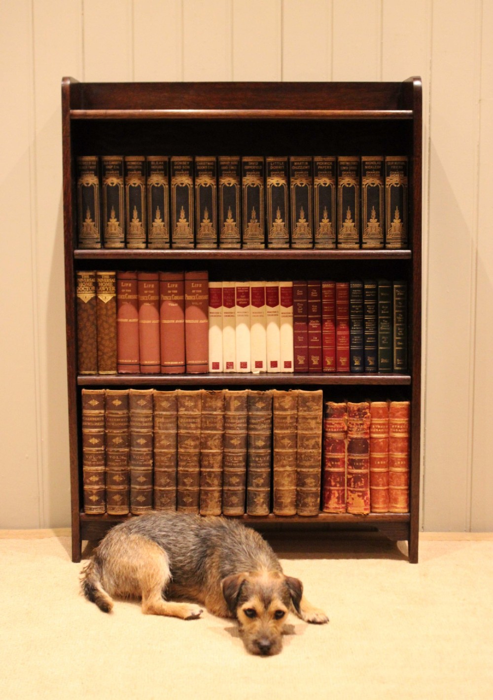 A dark brown oak open bookcase with three adjustable shelves, filled with vintage leather-bound books against a neutral panelled wall. View VIII