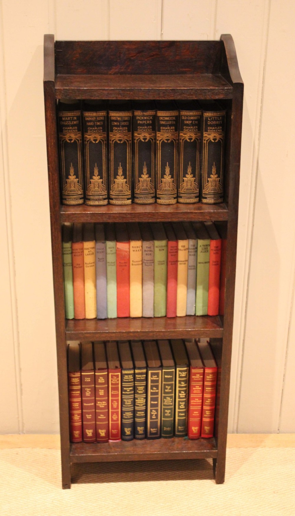 A small dark oak open bookcase featuring three open shelves filled with books and shaped side gallery panels at the top.