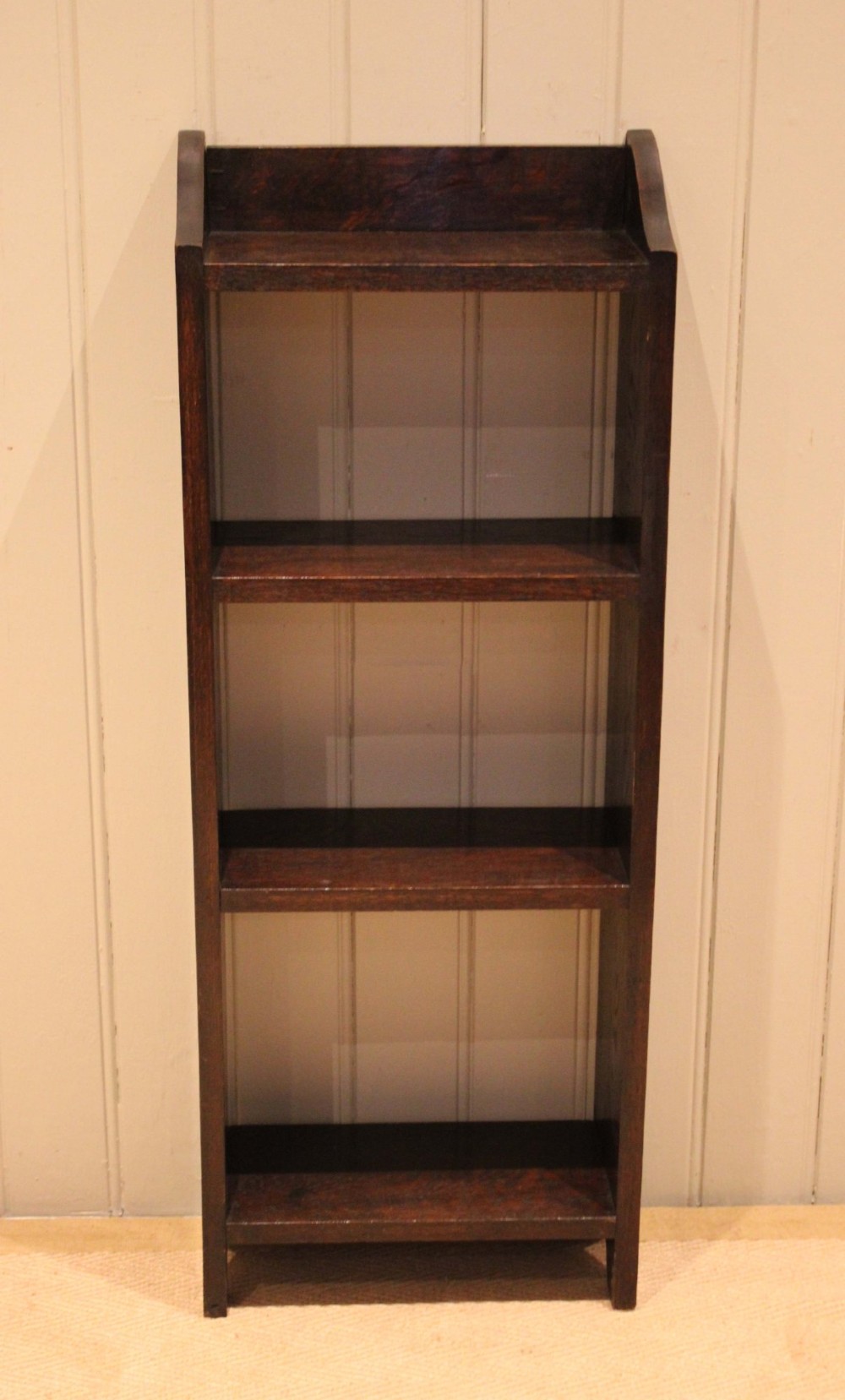 A small dark oak open bookcase featuring three open shelves filled with books and shaped side gallery panels at the top. View II
