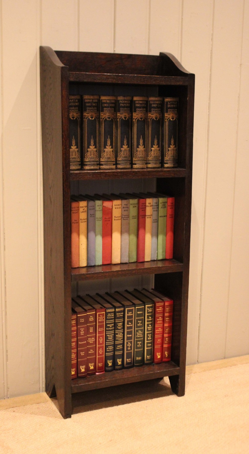 A small dark oak open bookcase featuring three open shelves filled with books and shaped side gallery panels at the top. View III