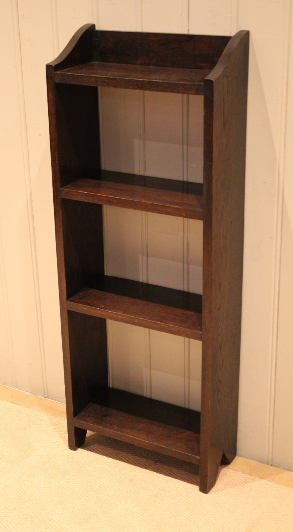 A small dark oak open bookcase featuring three open shelves filled with books and shaped side gallery panels at the top. View IV