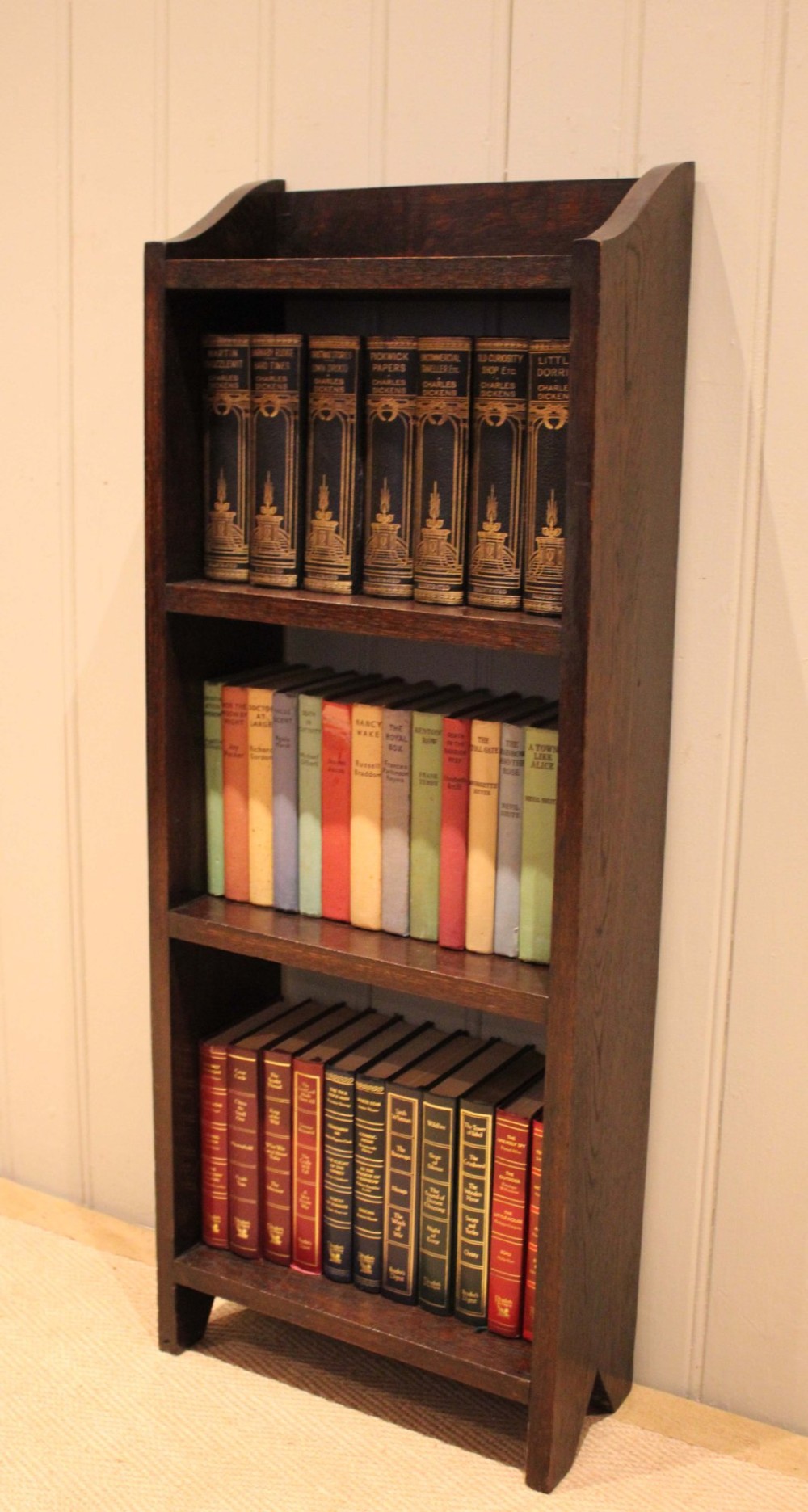A small dark oak open bookcase featuring three open shelves filled with books and shaped side gallery panels at the top. View V