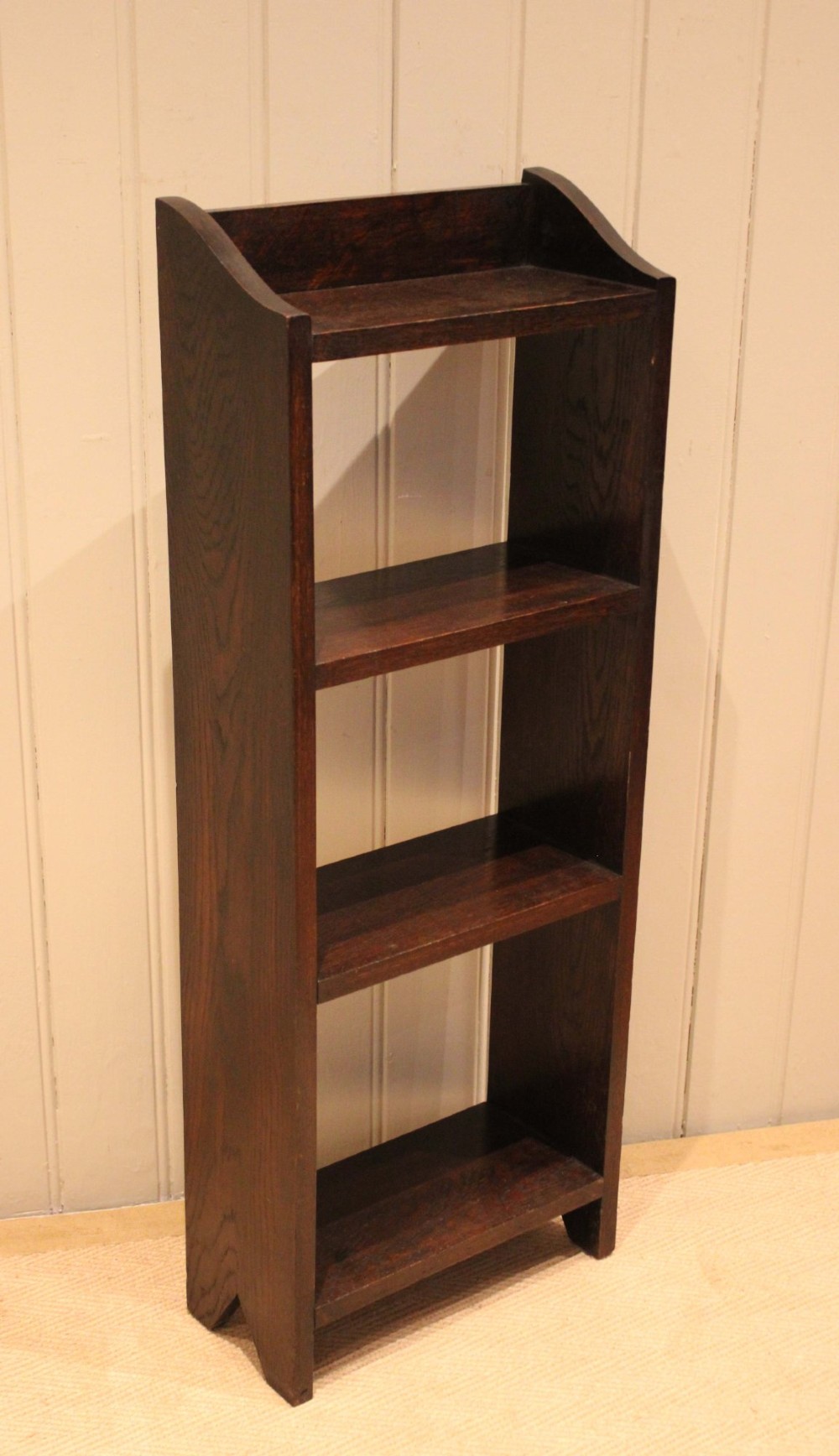 A small dark oak open bookcase featuring three open shelves filled with books and shaped side gallery panels at the top. View VI