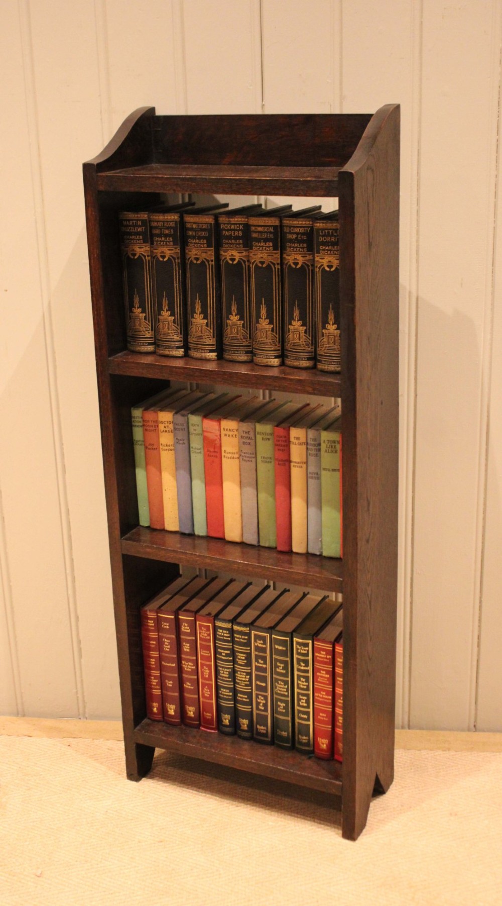 A small dark oak open bookcase featuring three open shelves filled with books and shaped side gallery panels at the top. View IX
