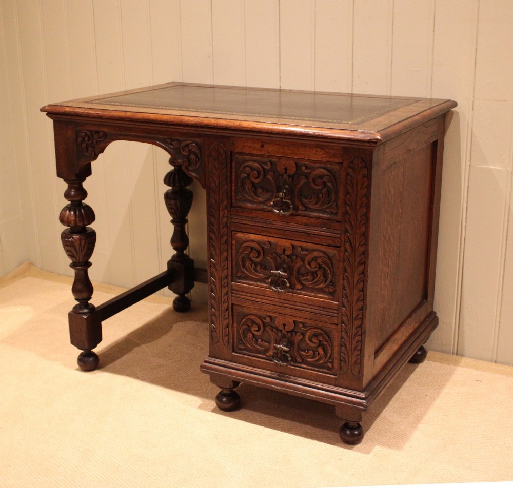 A late nineteenth-century dark carved oak writing desk featuring three side drawers with detailed foliate carvings and a leather inset writing surface. View V