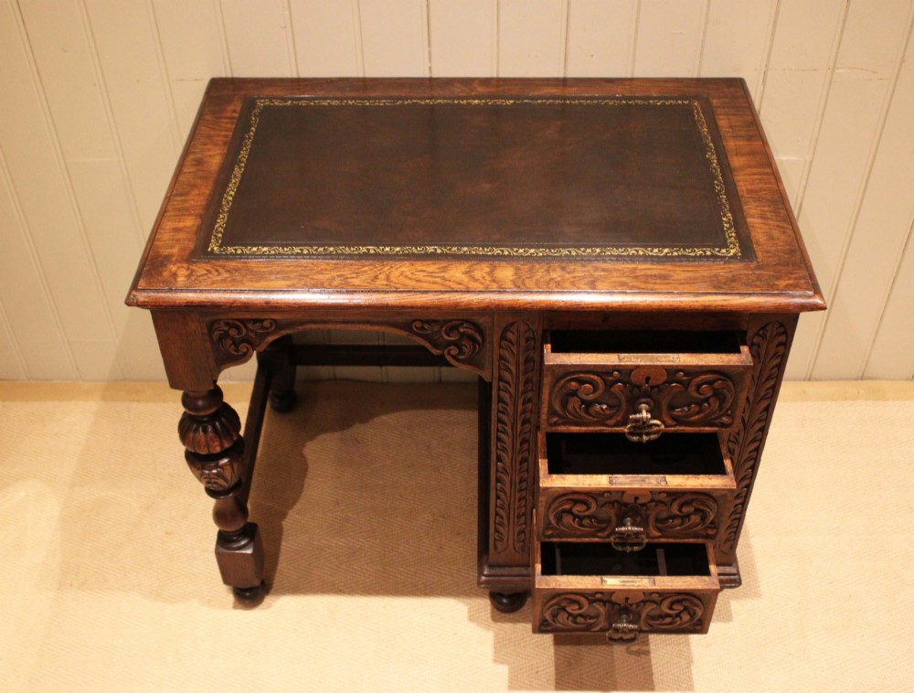 A late nineteenth-century dark carved oak writing desk featuring three side drawers with detailed foliate carvings and a leather inset writing surface. View VI