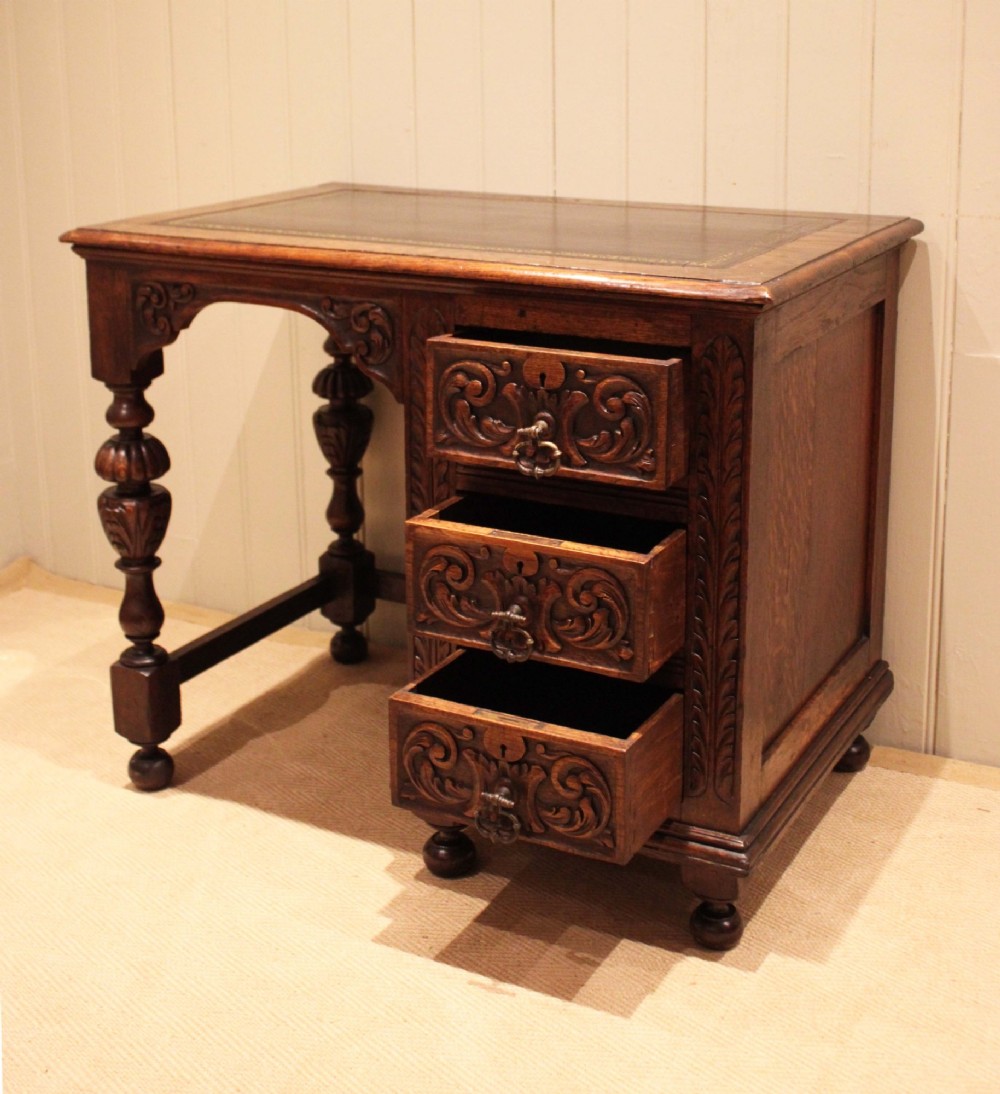 A late nineteenth-century dark carved oak writing desk featuring three side drawers with detailed foliate carvings and a leather inset writing surface. View VIII
