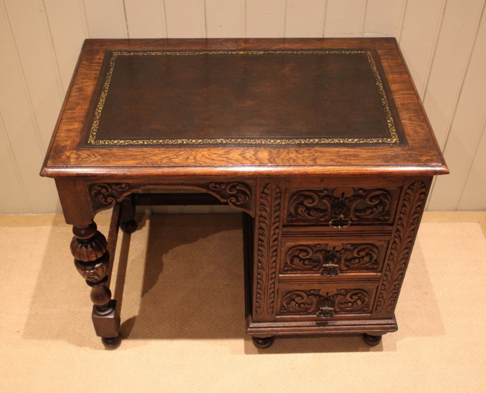 A late nineteenth-century dark carved oak writing desk featuring three side drawers with detailed foliate carvings and a leather inset writing surface. View IX